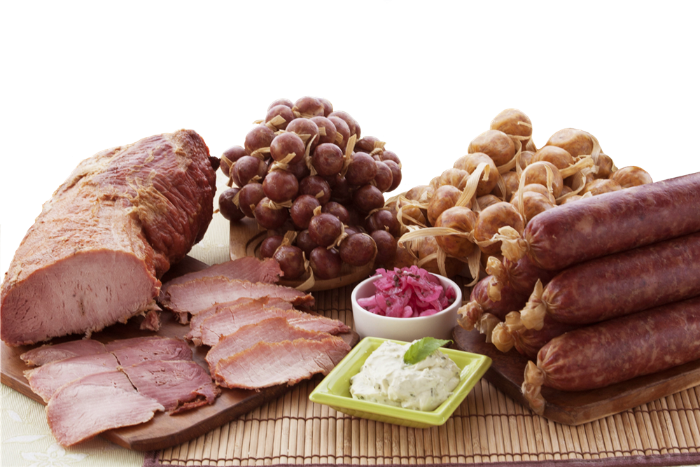 Familia completa de productos Doña Evita sobre petate: lomito de cerdo rebanado, butifarras y chorizos atados con tuza, salchichones, cebollita morada y dip de cilantro